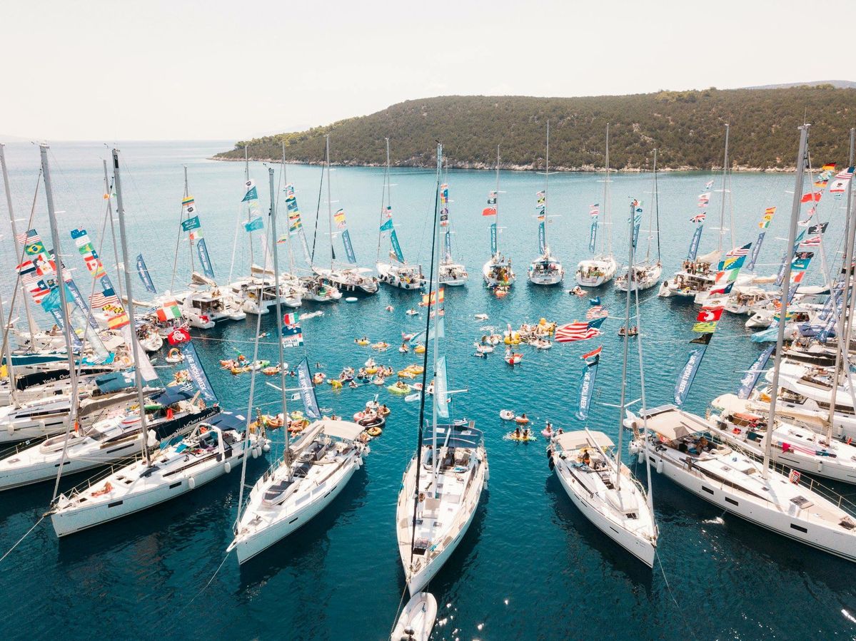 A raft-up of sailing yachts anchored together in a turquoise Mediterranean bay